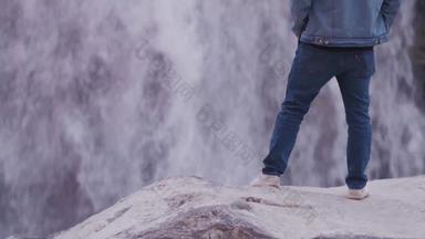 年轻的印度男人。站岩石自信地瀑布穿蓝色的牛仔布夹克蓝色的牛仔裤